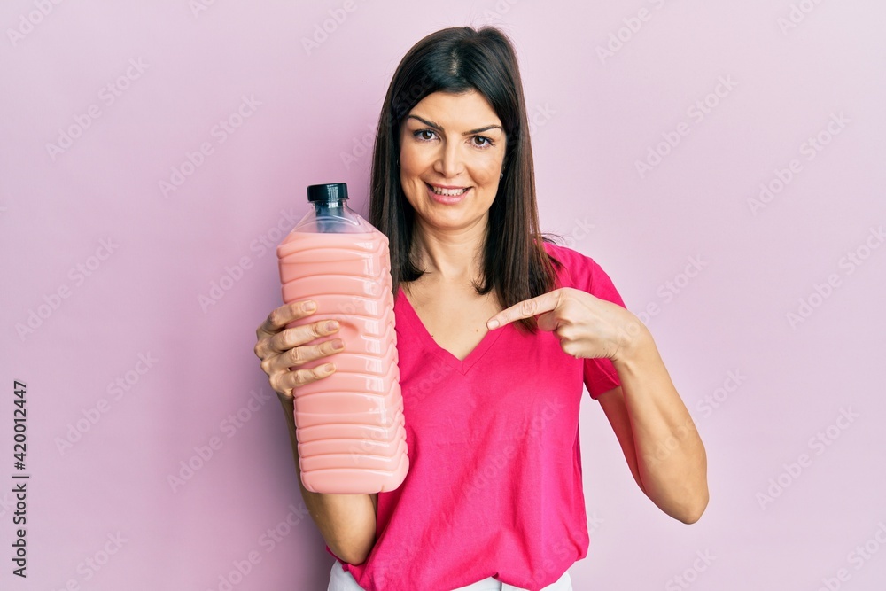 Young hispanic woman holding laundry softener bottle smiling happy pointing with hand and finger Young hispanic woman holding laundry softener bottle smiling happy pointing with hand and finger