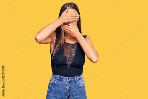 Young hispanic woman wearing casual clothes covering eyes and mouth with hands, surprised and shocked. hiding emotion © Krakenimages.com