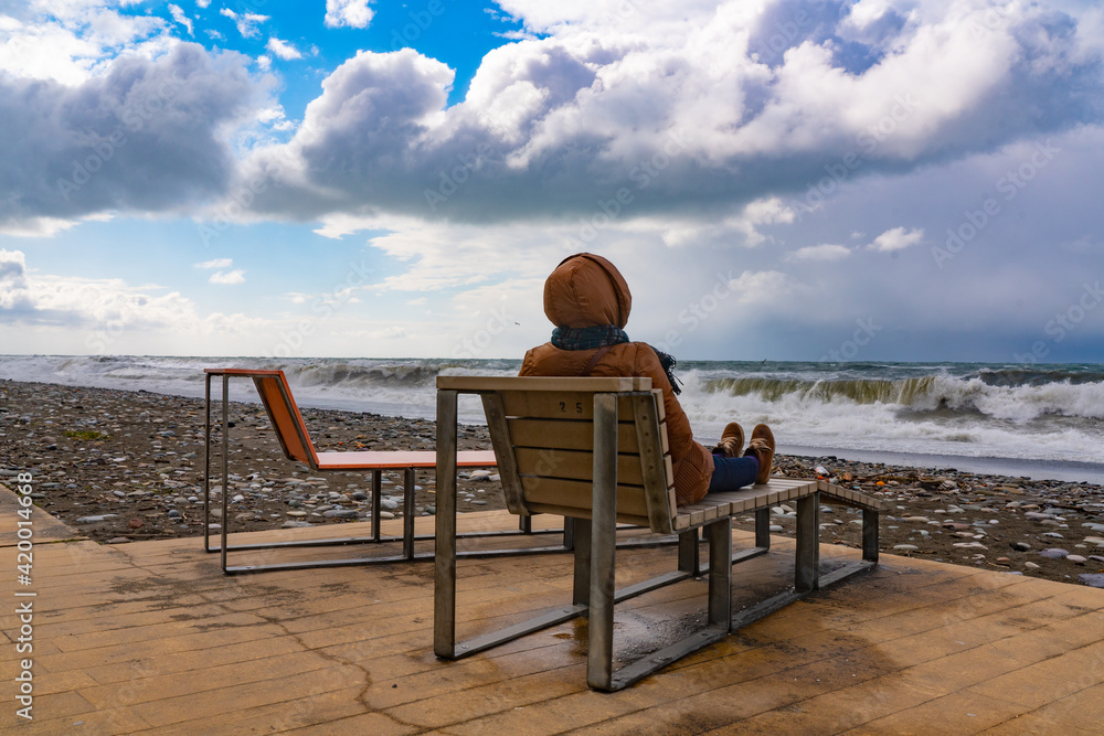 Woman sits on a bench by the sea during a storm