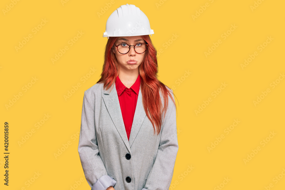 Young redhead woman wearing architect hardhat depressed and worry for distress, crying angry and afraid. sad expression.