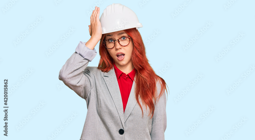 Young redhead woman wearing architect hardhat surprised with hand on head for mistake, remember error. forgot, bad memory concept. Young redhead woman wearing architect hardhat surprised with hand on head for mistake, remember error. forgot, bad memory concept.