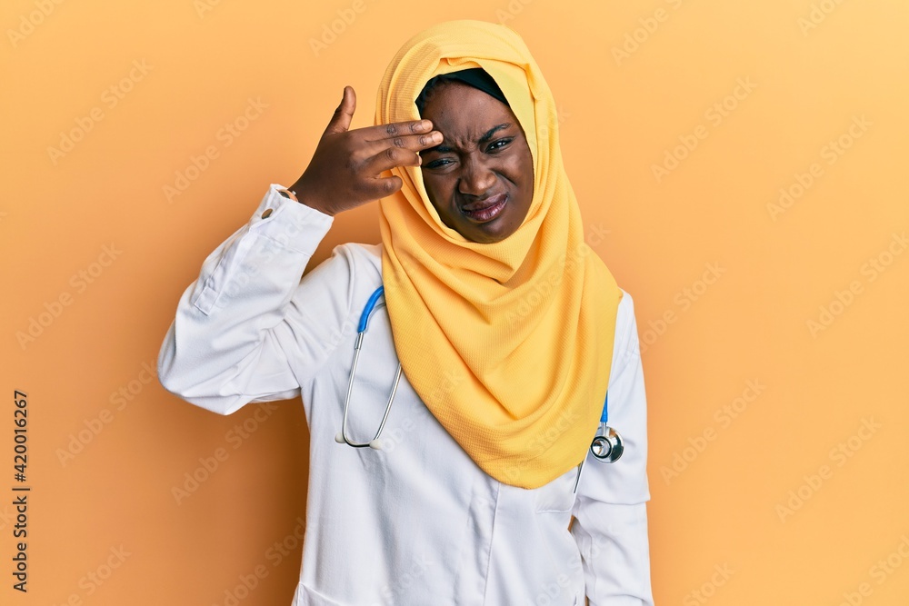 Beautiful african young woman wearing doctor uniform and hijab pointing unhappy to pimple on forehead, ugly infection of blackhead. acne and skin problem Beautiful african young woman wearing doctor uniform and hijab pointing unhappy to pimple on forehead, ugly infection of blackhead. acne and skin problem