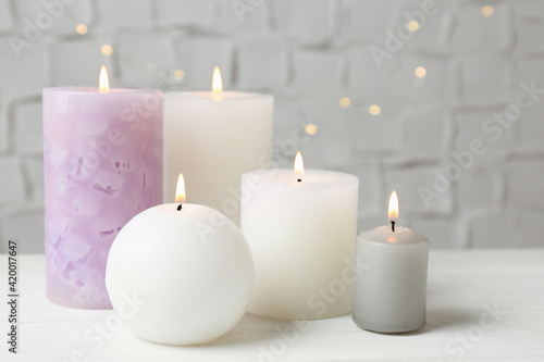 Set of different candles burning on white table