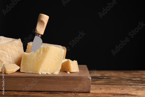 Parmesan cheese with knife on wooden table, closeup. Space for text