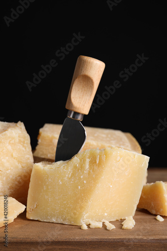 Parmesan cheese with knife on wooden board, closeup