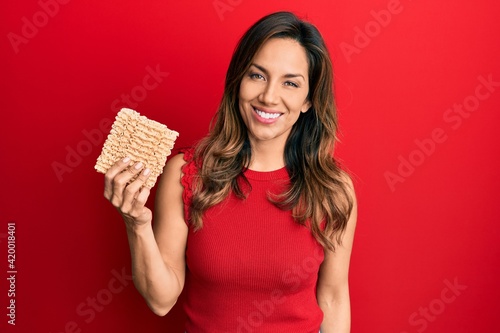 Young latin woman holding uncooked noodles looking positive and happy standing and smiling with a confident smile showing teeth