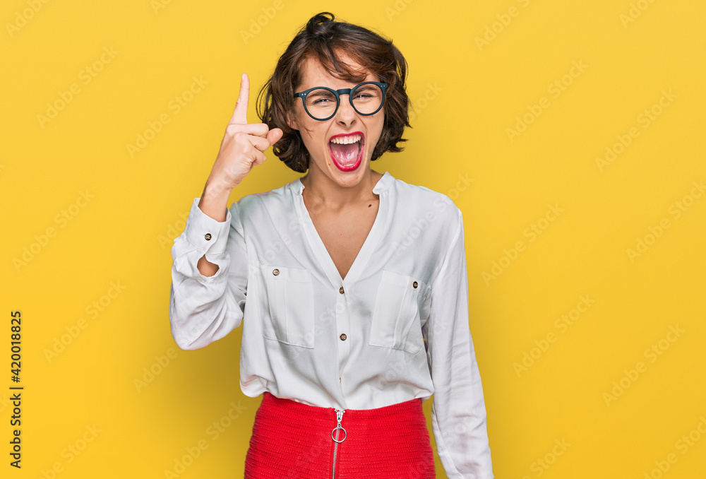Young hispanic woman wearing business style and glasses pointing finger up with successful idea. exited and happy. number one. Young hispanic woman wearing business style and glasses pointing finger up with successful idea. exited and happy. number one.