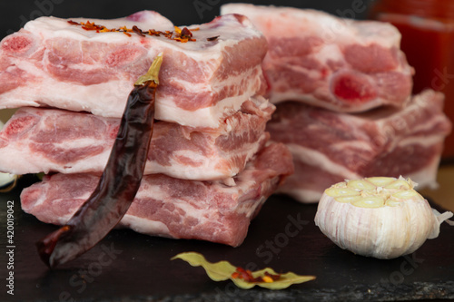 Raw pork ribs stacked with ingredients for cooking. Pepper, garlic, onion, tomato sauce and mustard.