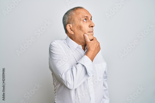 Handsome senior man wearing casual white shirt with hand on chin thinking about question, pensive expression. smiling with thoughtful face. doubt concept.