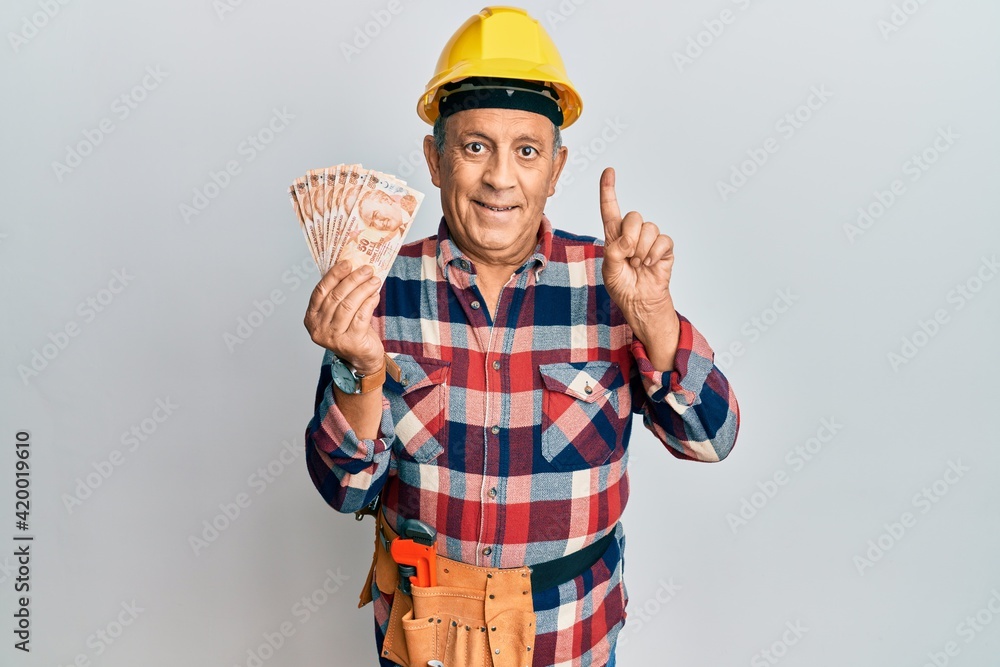 Senior hispanic man wearing handyman uniform holding turkish liras smiling with an idea or question pointing finger with happy face, number one