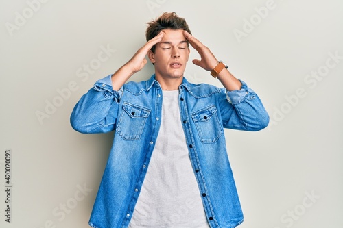 Handsome caucasian man wearing casual denim jacket with hand on head, headache because stress. suffering migraine.