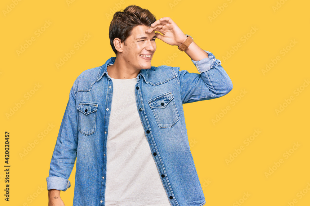 Handsome caucasian man wearing casual denim jacket very happy and smiling looking far away with hand over head. searching concept. Handsome caucasian man wearing casual denim jacket very happy and smiling looking far away with hand over head. searching concept.