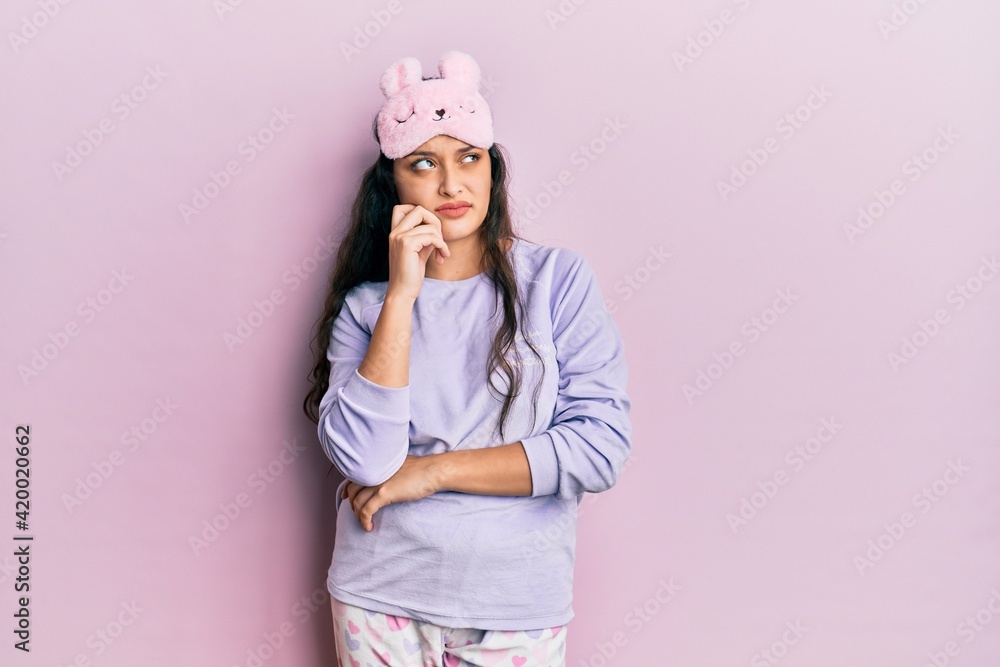 Beautiful middle eastern woman wearing sleep mask and pajama serious face thinking about question with hand on chin, thoughtful about confusing idea Beautiful middle eastern woman wearing sleep mask and pajama serious face thinking about question with hand on chin, thoughtful about confusing idea