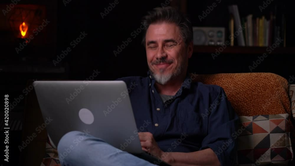 Man sitting on couch at home with laptop computer, talking on video chat. Businessman working in home office. Portrait of mature age, middle age, mid adult man, bearded, authentic look. Man sitting on couch at home with laptop computer, talking on video chat. Businessman working in home office. Portrait of mature age, middle age, mid adult man, bearded, authentic look.
