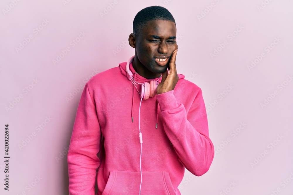 Young african american man wearing gym clothes and using headphones touching mouth with hand with painful expression because of toothache or dental illness on teeth. dentist Young african american man wearing gym clothes and using headphones touching mouth with hand with painful expression because of toothache or dental illness on teeth. dentist
