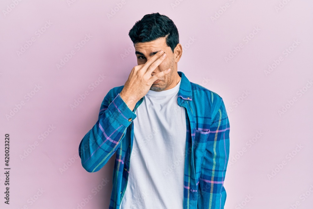 Fototapeta premium Handsome hispanic man wearing casual clothes smelling something stinky and disgusting, intolerable smell, holding breath with fingers on nose. bad smell