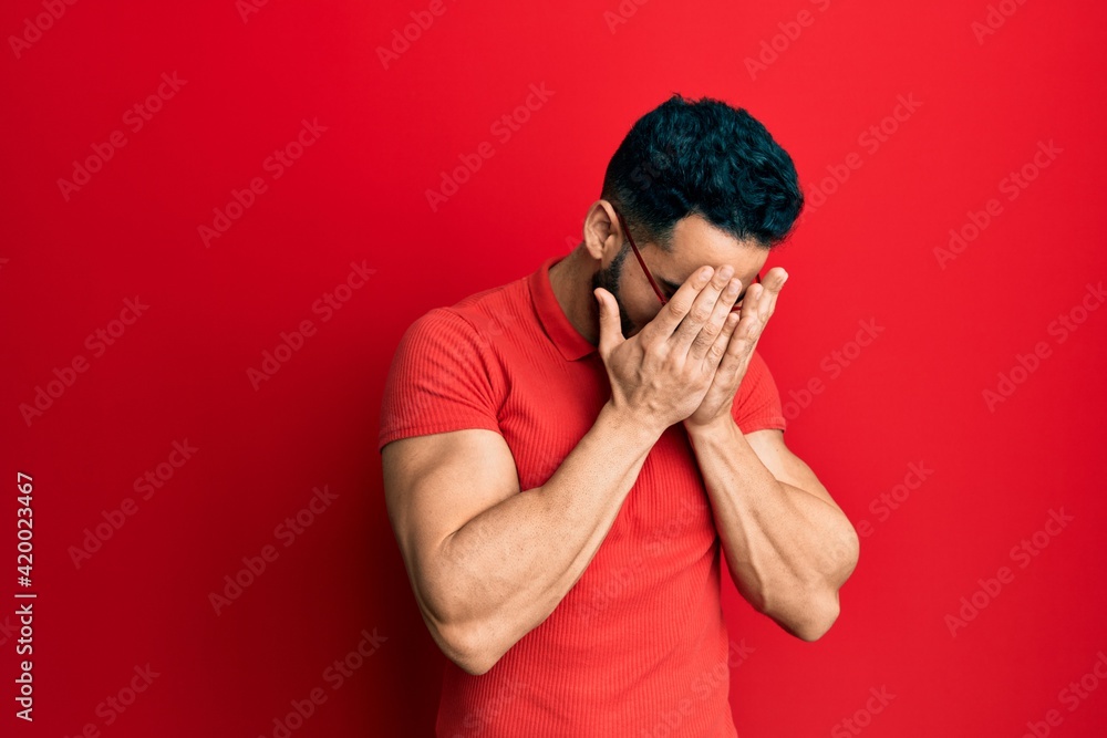 Young hispanic man wearing casual clothes and glasses with sad expression covering face with hands while crying. depression concept. Young hispanic man wearing casual clothes and glasses with sad expression covering face with hands while crying. depression concept.