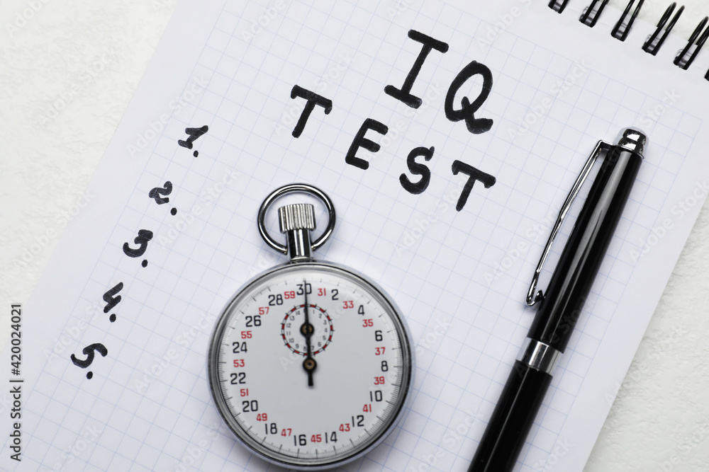 Notebook with words IQ Test, pen and timer on white table, top view Notebook with words IQ Test, pen and timer on white table, top view