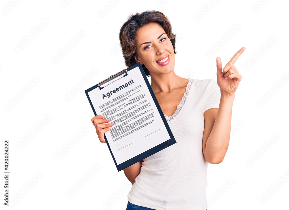 Young beautiful woman holding clipboard with agreement document smiling happy pointing with hand and finger to the side Young beautiful woman holding clipboard with agreement document smiling happy pointing with hand and finger to the side