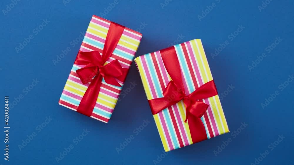 colorful wrapped gift boxes with red ribbon bows move on a blue background, top view, stop motion animation colorful wrapped gift boxes with red ribbon bows move on a blue background, top view, stop motion animation