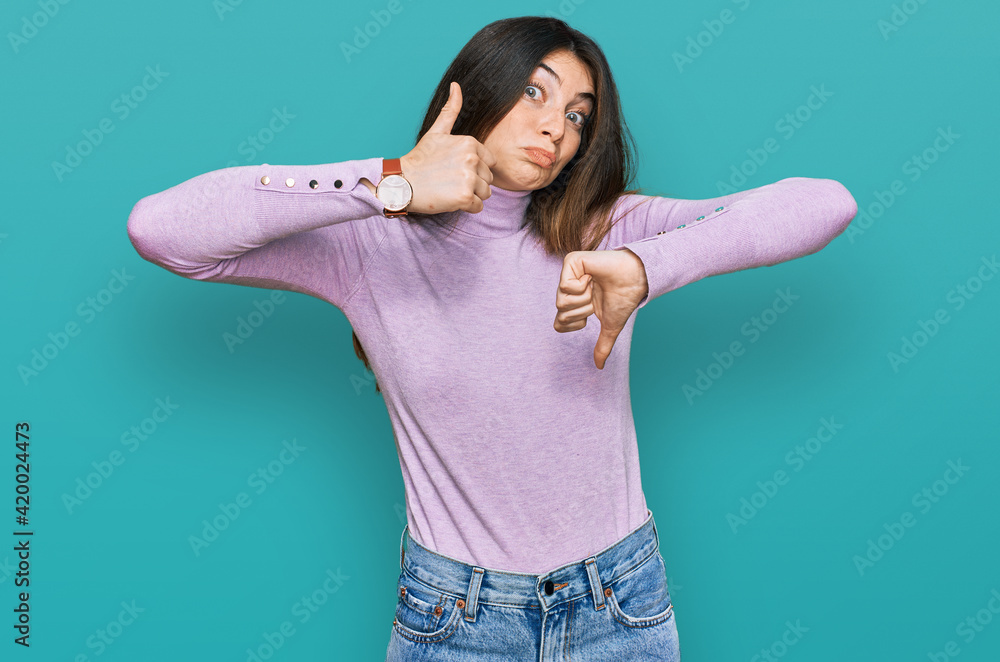 Young beautiful teen girl wearing turtleneck sweater doing thumbs up and down, disagreement and agreement expression. crazy conflict Young beautiful teen girl wearing turtleneck sweater doing thumbs up and down, disagreement and agreement expression. crazy conflict