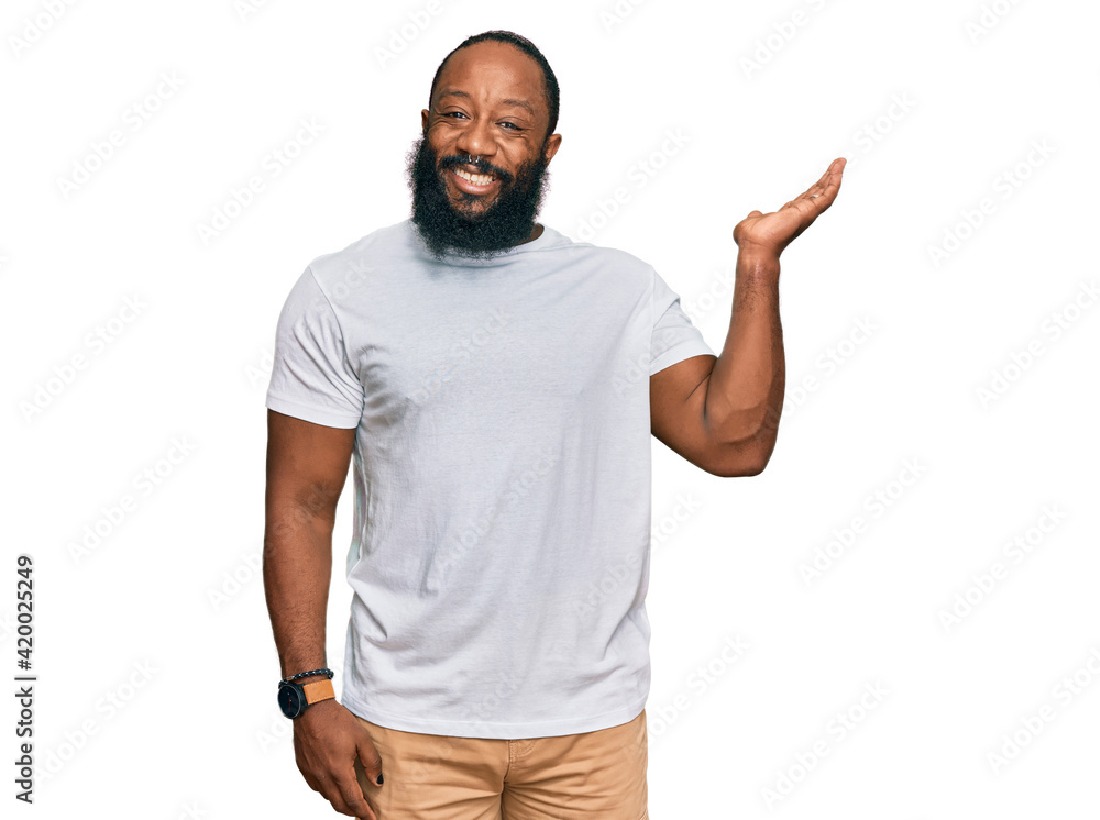 Young african american man wearing casual white tshirt smiling cheerful presenting and pointing with palm of hand looking at the camera.