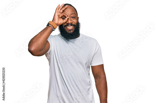 Young african american man wearing casual white tshirt doing ok gesture with hand smiling, eye looking through fingers with happy face.