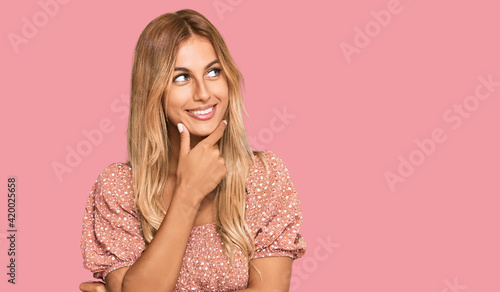 Beautiful blonde young woman wearing summer top with hand on chin thinking about question, pensive expression. smiling with thoughtful face. doubt concept.