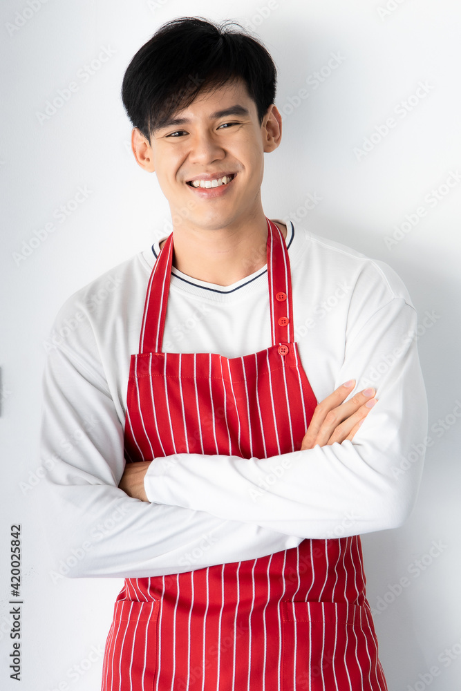 Cute, young and handsome Asian man wearing apron standing and cross arms with self-confident Cute, young and handsome Asian man wearing apron standing and cross arms with self-confident
