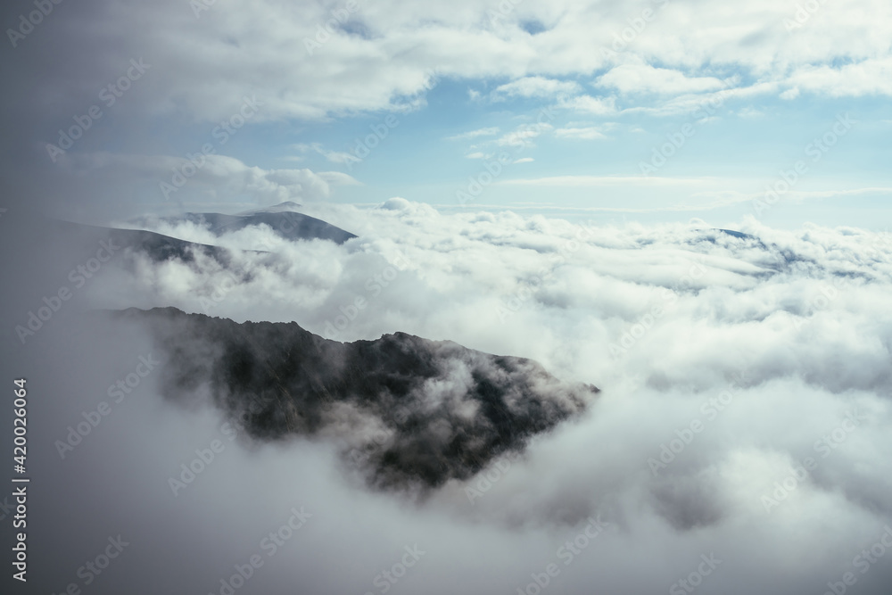 Wonderful alpine scenery with great rocks and mountains in dense low clouds. Atmospheric highlands landscape with mountain tops above clouds. Beautiful view to snow mountain peaks over thick clouds.