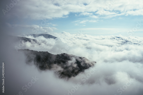 Wonderful alpine scenery with great rocks and mountains in dense low clouds. Atmospheric highlands landscape with mountain tops above clouds. Beautiful view to snow mountain peaks over thick clouds.