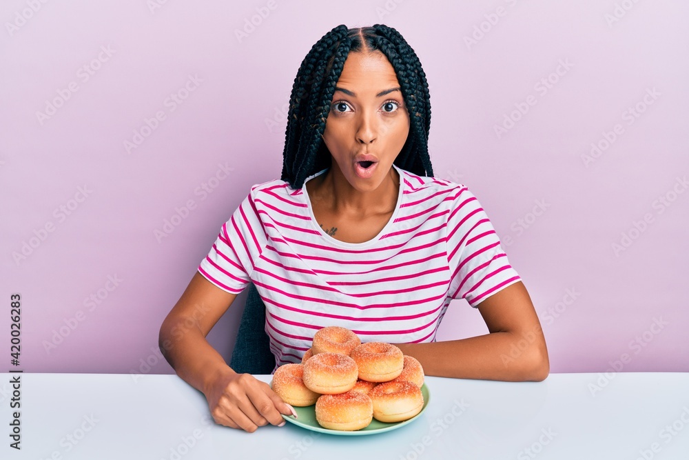 Beautiful hispanic woman eating doughnut for breakfast scared and amazed with open mouth for surprise, disbelief face Beautiful hispanic woman eating doughnut for breakfast scared and amazed with open mouth for surprise, disbelief face