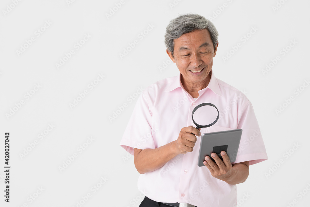 Portrait of a senior older Asian man holding and using magnifier glass to see and watch screen of tablet computer on white background. Idea for older people eyes health problem Portrait of a senior older Asian man holding and using magnifier glass to see and watch screen of tablet computer on white background. Idea for older people eyes health problem