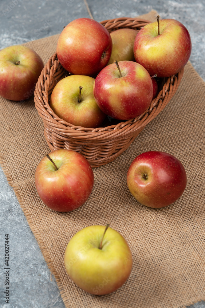 Wicker basket of ripe shiny apples on marble surface Wicker basket of ripe shiny apples on marble surface