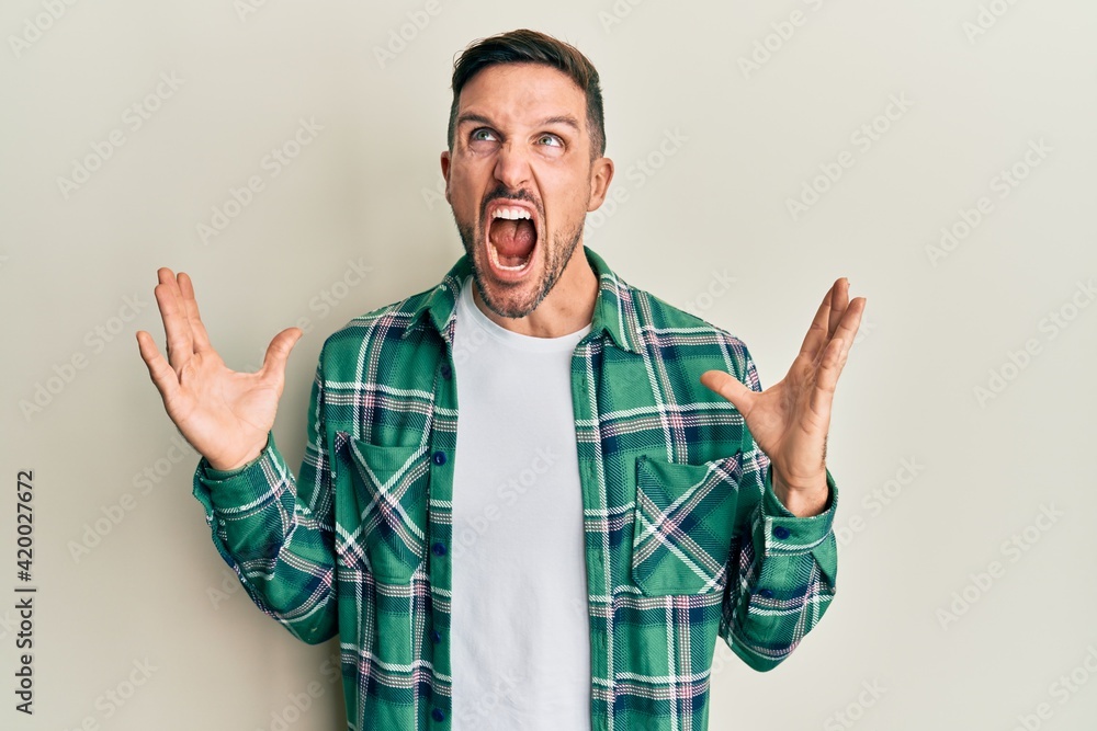 Handsome man with beard wearing casual clothes crazy and mad shouting and yelling with aggressive expression and arms raised. frustration concept. Handsome man with beard wearing casual clothes crazy and mad shouting and yelling with aggressive expression and arms raised. frustration concept.
