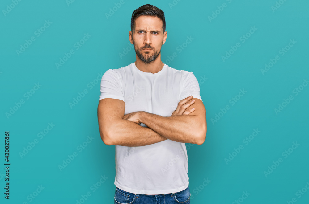 Handsome man with beard wearing casual white t shirt skeptic and nervous, disapproving expression on face with crossed arms. negative person. Handsome man with beard wearing casual white t shirt skeptic and nervous, disapproving expression on face with crossed arms. negative person.