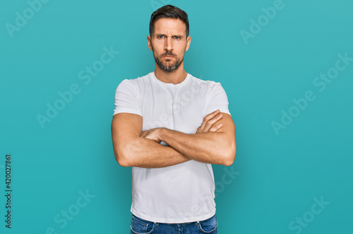 Handsome man with beard wearing casual white t shirt skeptic and nervous, disapproving expression on face with crossed arms. negative person.