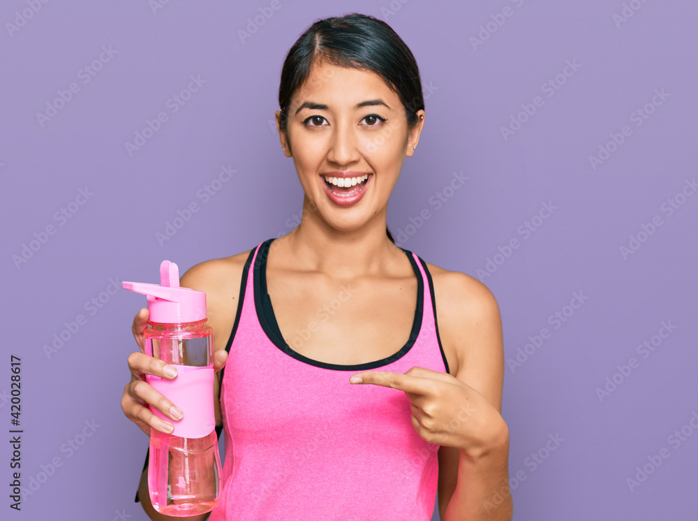 Beautiful asian young sport woman wearing sportswear drinking bottle of water smiling happy pointing with hand and finger Beautiful asian young sport woman wearing sportswear drinking bottle of water smiling happy pointing with hand and finger