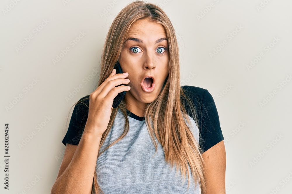 Young blonde woman having conversation talking on the smartphone scared and amazed with open mouth for surprise, disbelief face Young blonde woman having conversation talking on the smartphone scared and amazed with open mouth for surprise, disbelief face