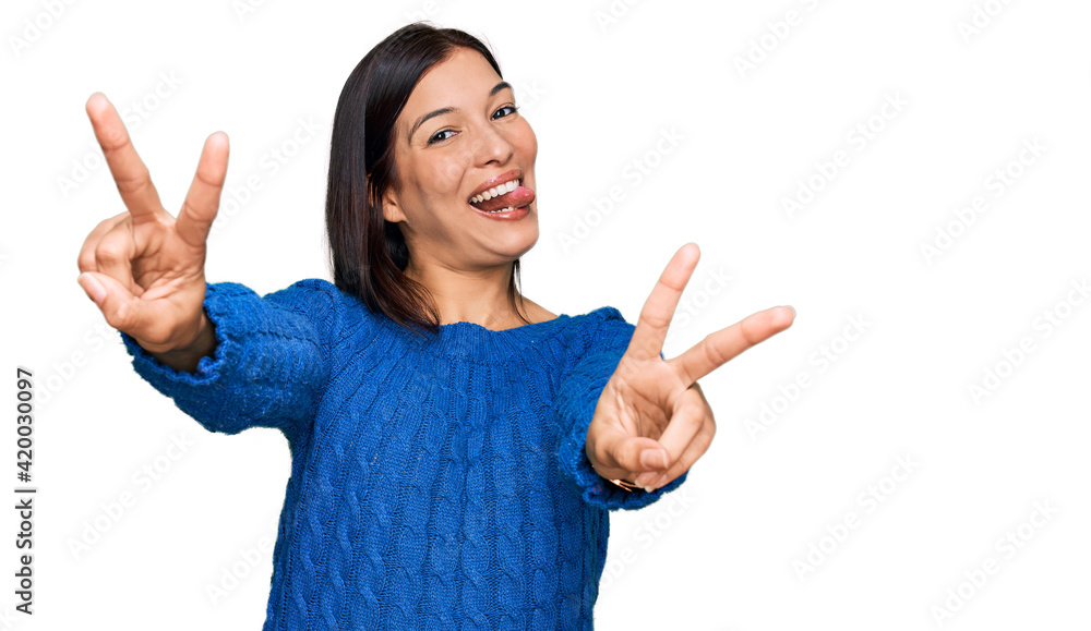 Young hispanic woman wearing casual clothes smiling with tongue out showing fingers of both hands doing victory sign. number two. Young hispanic woman wearing casual clothes smiling with tongue out showing fingers of both hands doing victory sign. number two.