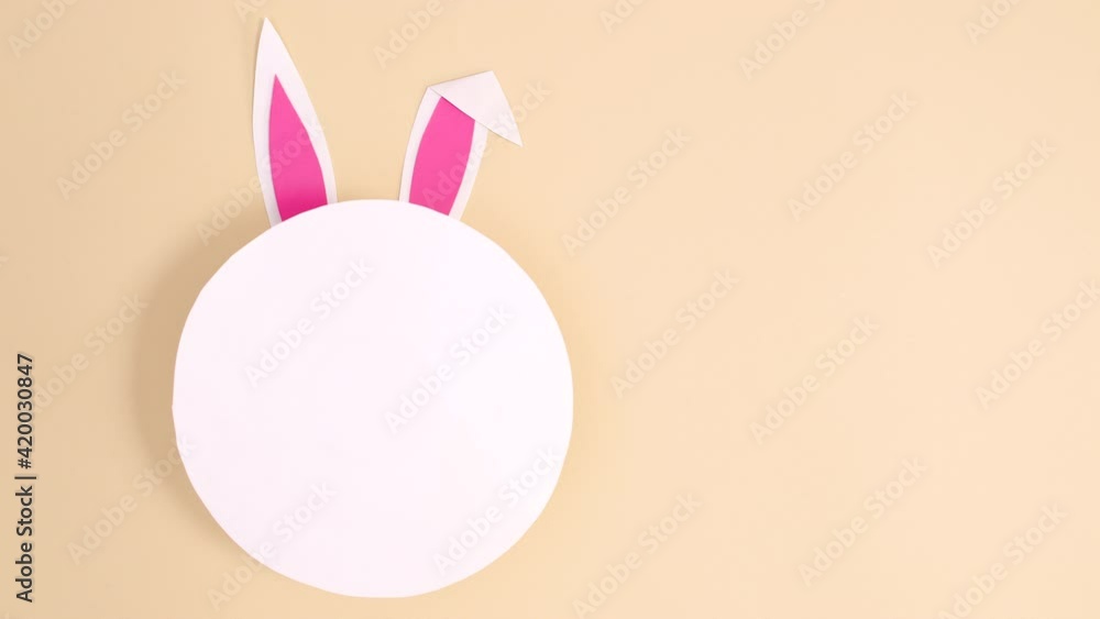 Creative Easter bunny with ears appear under round paper card note on nude background. Minimal flat lay stop motion Creative Easter bunny with ears appear under round paper card note on nude background. Minimal flat lay stop motion