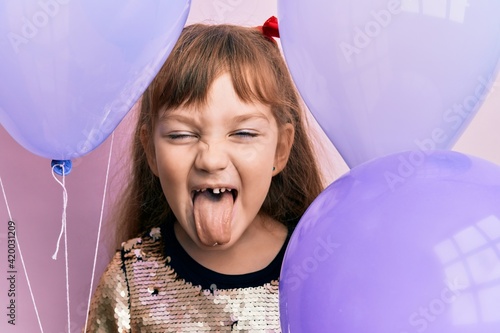 Little caucasian girl kid holding balloons sticking tongue out happy with funny expression. photo