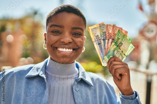 Young african american woman smiling happy holding south africa rand banknotes at the city. photo