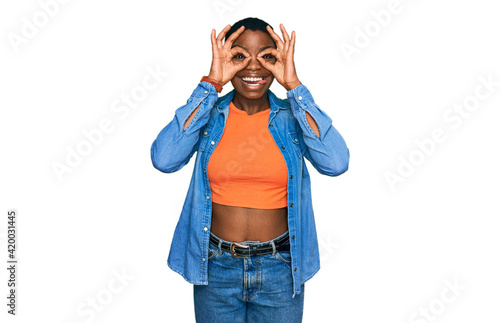 Young african american woman wearing casual clothes doing ok gesture like binoculars sticking tongue out, eyes looking through fingers. crazy expression.