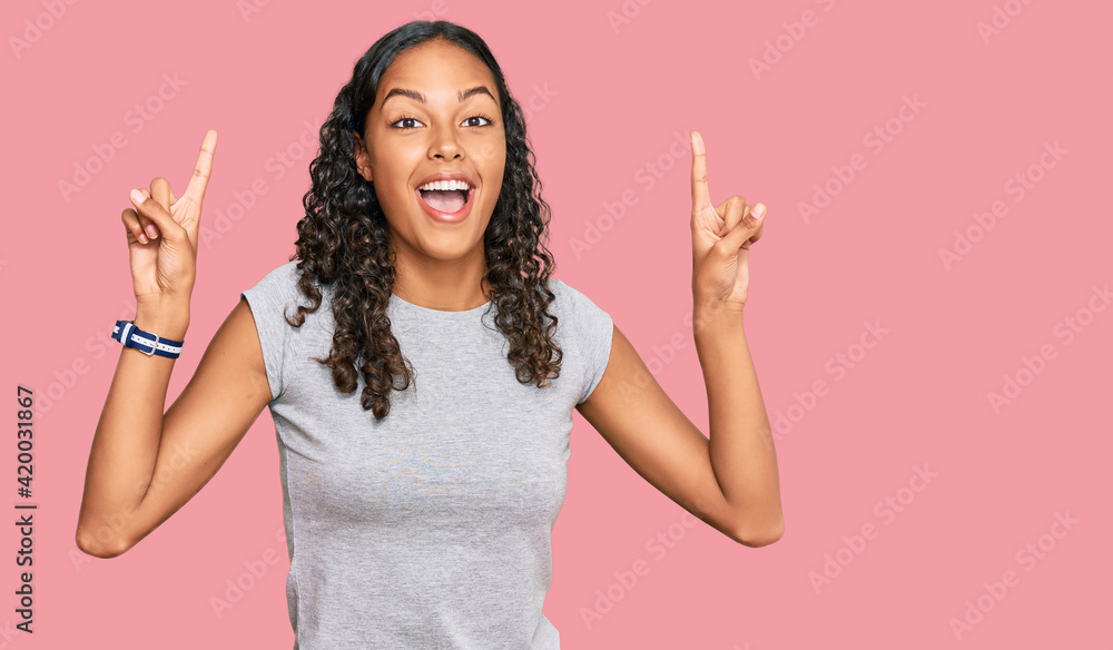 Young african american girl wearing casual clothes smiling amazed and surprised and pointing up with fingers and raised arms. Young african american girl wearing casual clothes smiling amazed and surprised and pointing up with fingers and raised arms.