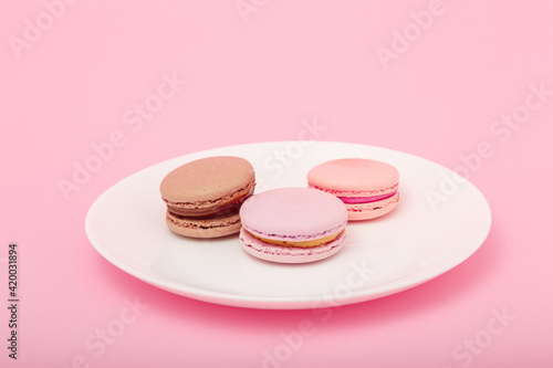 three macaroons on white plate on pink paper background. Sweet bakery, copy space. Overweight, diet, diabetes, healthy eating habits.