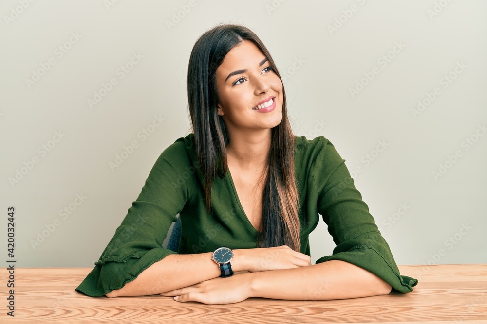 Young brunette woman wearing casual clothes sitting on the table looking away to side with smile on face, natural expression. laughing confident. Young brunette woman wearing casual clothes sitting on the table looking away to side with smile on face, natural expression. laughing confident.