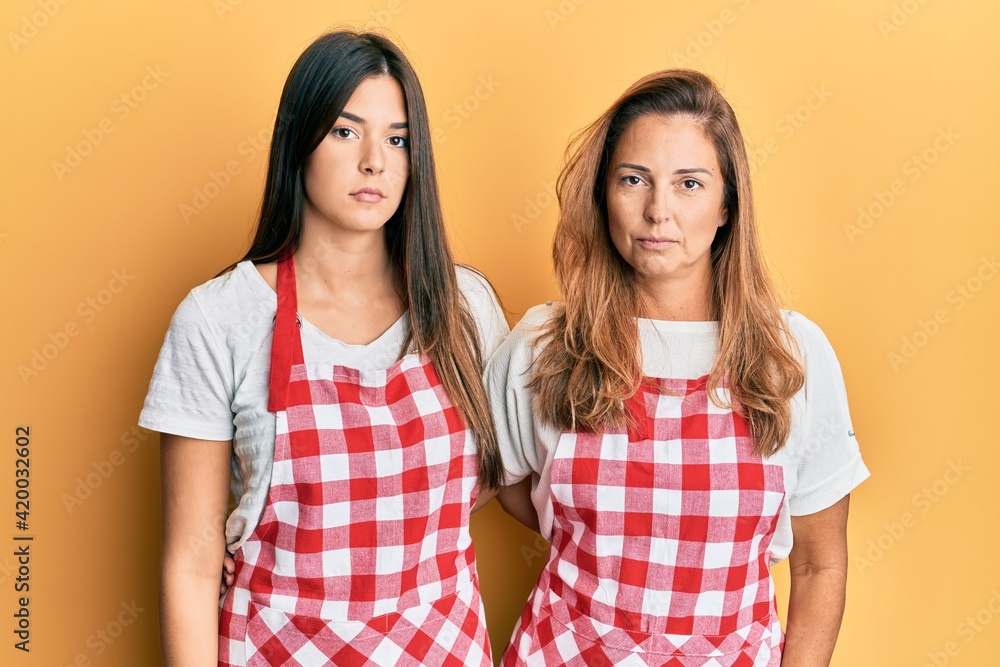 Hispanic family of mother and daughter wearing baker uniform over yellow background thinking attitude and sober expression looking self confident Hispanic family of mother and daughter wearing baker uniform over yellow background thinking attitude and sober expression looking self confident