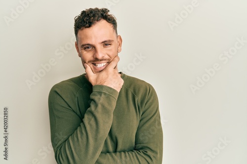 Young hispanic man wearing casual clothes looking confident at the camera smiling with crossed arms and hand raised on chin. thinking positive.