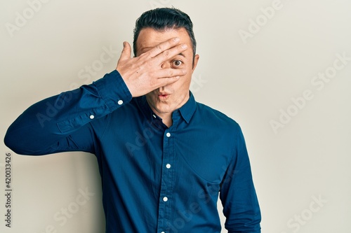 Handsome young man wearing business shirt peeking in shock covering face and eyes with hand, looking through fingers afraid